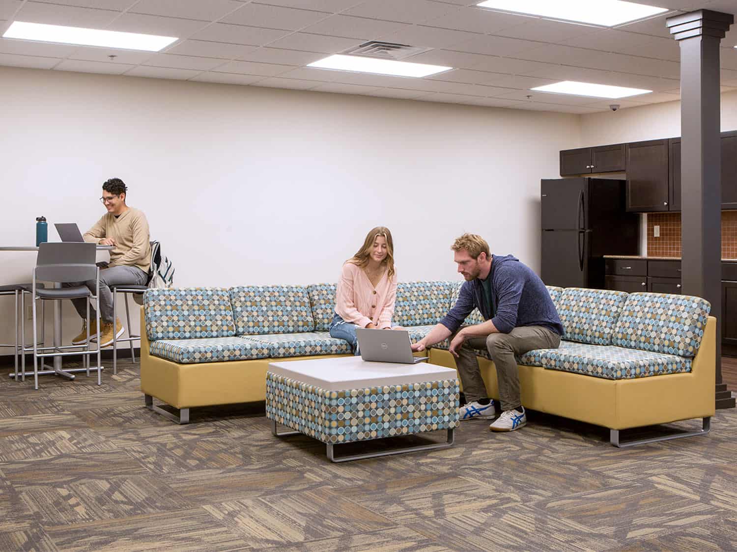 Students in lounge area studying on Rally Modular Seating and at a Tubular Table with Upland Metal Bar Stools..