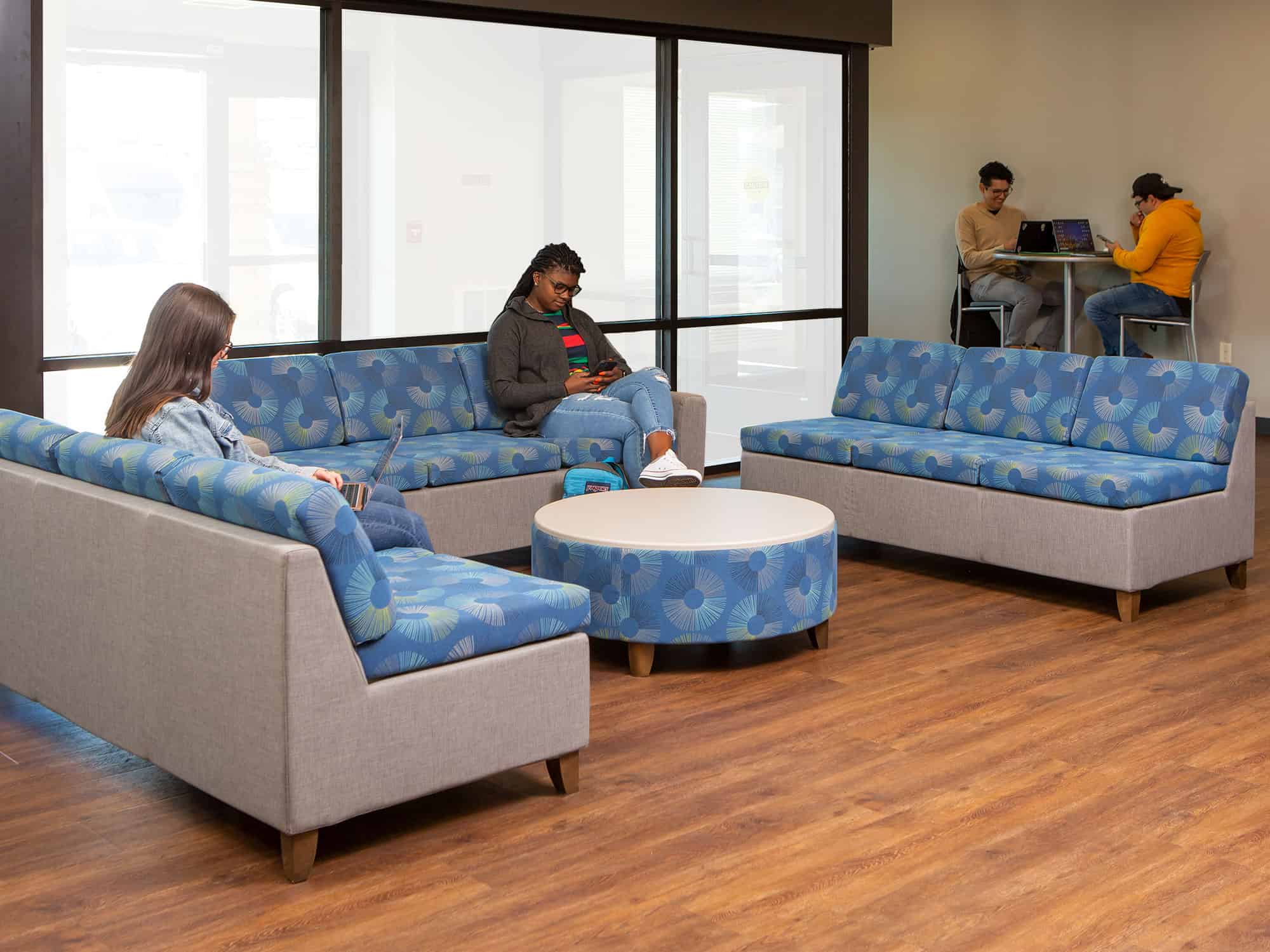 Students sitting in lounge area on Rally Modular Furniture while others study at a a Multi-Purpose Table while sitting in Barstools.